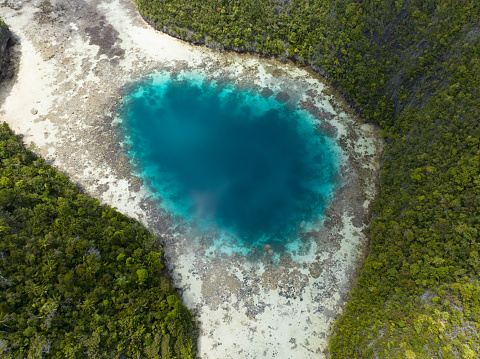 A blue hole is found amid the limestone seascape in Misool, Raja Ampat, Indonesia. These scenic islands' coral reefs, and the surrounding seas, support extraordinary marine biodiversity.