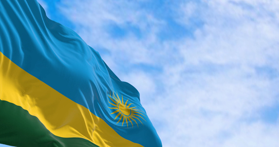 Close-up of Rwanda national flag waving on a clear day. 3 horizontal bands: blue, yellow, green with 24 rays yellow sun. 3d illustration render. Selective focus