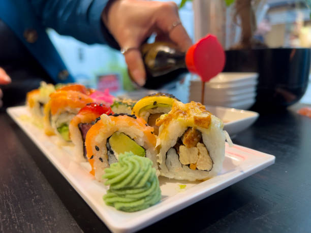 Colourful plate with many different tasty sushi rolls behind a decorated piece of wasabi cream on a white plate over a black table. Asian food background, copy space.