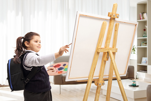Schoolgirl painting on a canvas inside a room