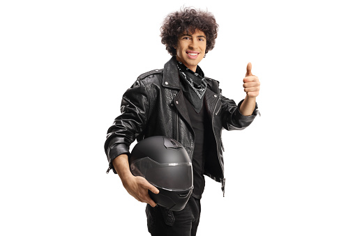 Young man in a black leather jacket holding a helmet and gesturing thumbs up isolated on white background