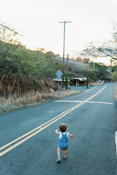 Rear view of an Eurasian one year old boy running with excitement down the road in front of his home in a rural residential neighborhood in Hawaii during a Halloween block party on a beautiful and warm Autumn evening.