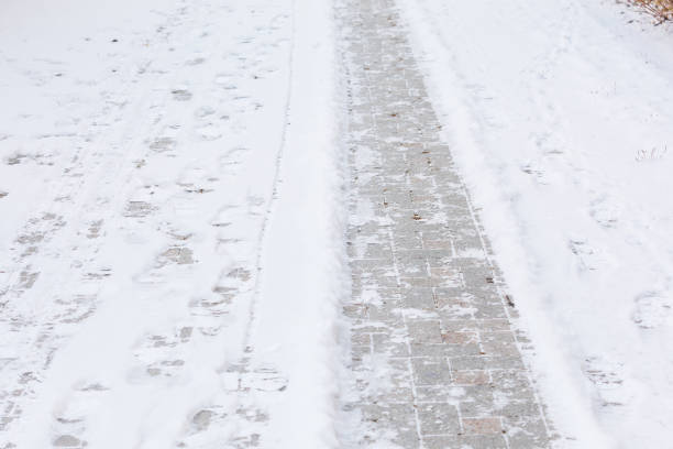 Stone urban pavement is covered with frosty snow and ice. Winter background of frozen tiled sidewalk.
