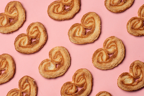 Puff pastry biscuits pattern. Salty, soft, baked pretzels lined up on a pastel pink background