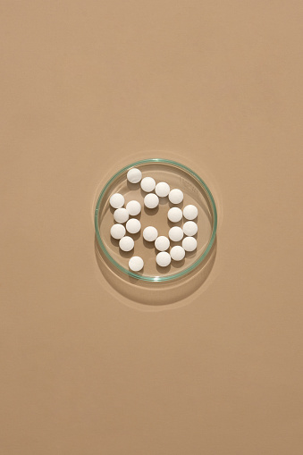 The round white pills are displayed on a transparent petri dish on a brown background. Antibiotics with bactericidal activity may improve bacterial killing.