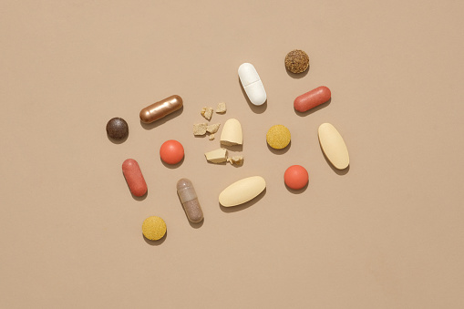 Top view of a broken pill in the middle, surrounded by pills of different colors and shapes on a brown background. Creative space for advertising.