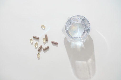 A glass of water on a white background with capsules. Capsule medicine is a form of divided dosage medicine with ingredients including capsule shell (made of starch, gelatin, HPMC, ...).