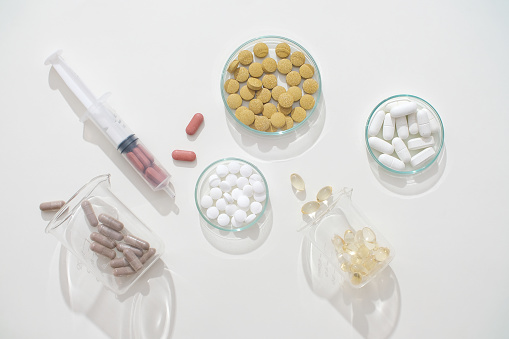 Pills of different shapes and colors are contained in transparent glassware on a white background. Medicines exert their effects in the body through different mechanisms.