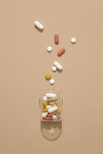 Pills of different colors and shapes are contained in a transparent glass jar. Some pills were spread on the table. Medicines bring many benefits during treatment.