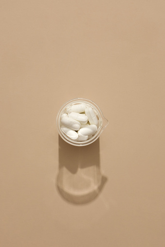 View from above of a glass jar of white pills on a minimalist background. Copy space for drug advertising. Medicines can diagnose and prevent diseases and significantly improve symptoms.