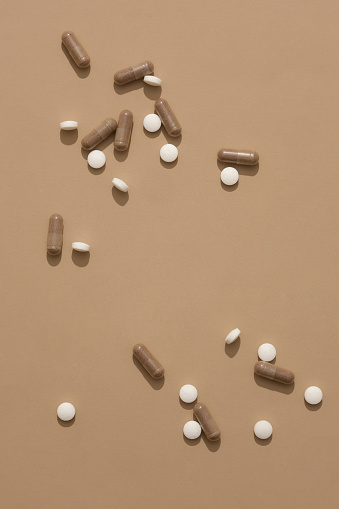 Round white pills along with brown capsules are displayed on a pastel brown background. Free space for display and design. Copy space for drug advertising.