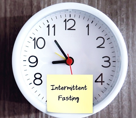 Wall clock with sticky note written INTERMITTEN FASTING, eating plan that switches between fasting and eating on regular schedule, eat only for a set of time