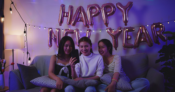 Selective focus, Portrait of Cheerful young asian woman and her female friends enjoy to use smartphone making video call together with fun at New Year's night party