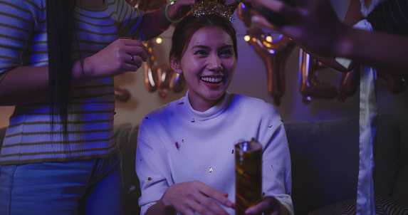 selective focus, young asian woman and beautiful female friend wears crown headband countdown to new year and use smartphone record video while enjoy celebration party together