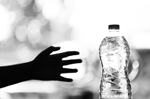 The shadow of a hand reaches towards a bottle of drinking water. black and white scene concept photo