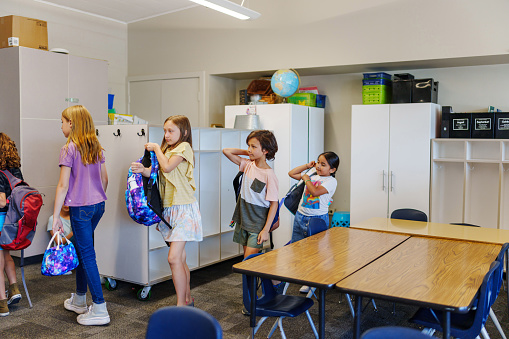 A multiracial group of elementary age students hold their backpacks and stand in line while waiting to leave their classroom at the end of the school day.