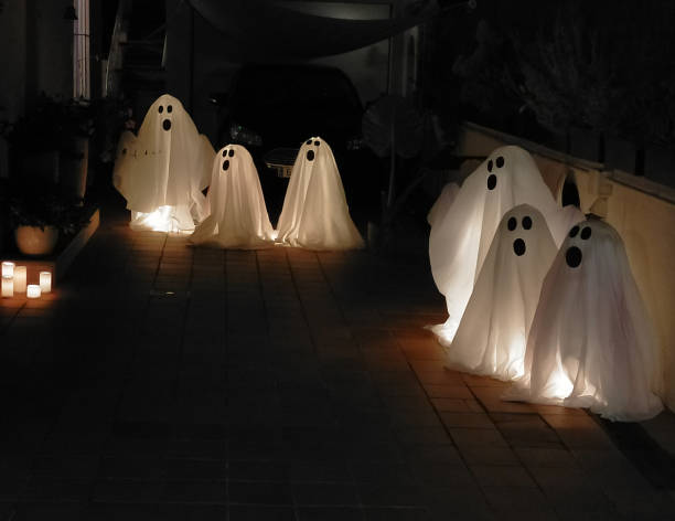 6 ghosts made by hand with white sheets and lighting inside, displayed on Halloween night with copy space
