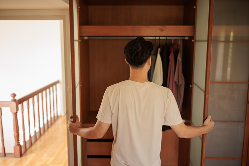 A young Asian man is opening the closet to take his work clothes in the bedroom in the morning.