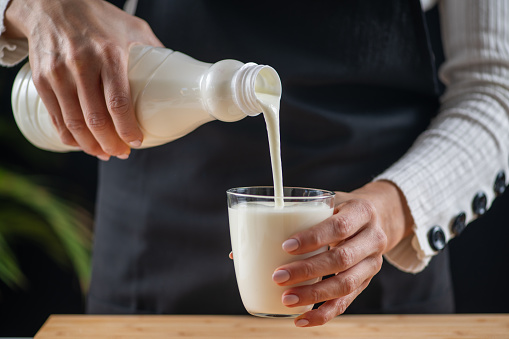 Close-up of pouring fresh milk in glass. Milk is being poured in a glass on the kitchen table at home.