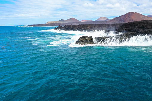 Aerial panorama view of Los Hervideros. Southwest coast, rugged volcanic coast, strong surf, sea caves, red lava hills. Lanzarote, Canary Islands, Spain