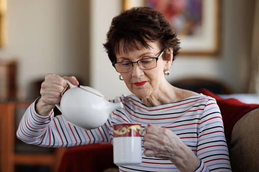 Smiling woman pouring tea into a mug from a pot, at home.