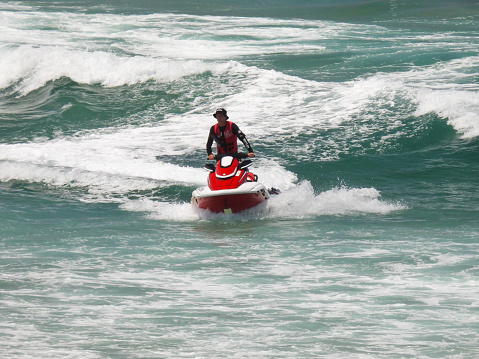 A lifeguard on a jet ski heads towards the shore during a patrol off Bondi Beach.  The jet ski is towing a raft or mat which people can hold onto if they are having difficulty in the water.  This image was taken on a hot and sunny afternoon on 25 December 2023.