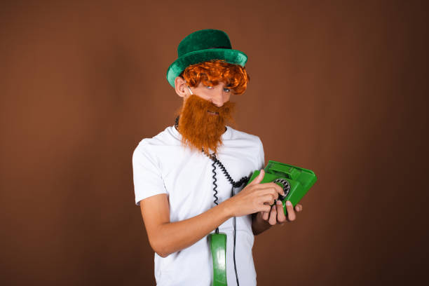 istock St.Patrick 's Day. Funny guy in a leprechaun costume posing on a brown background. 1889064260