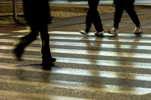 Blurred dark silhouettes of the people legs walking through the pedestrian crossing.