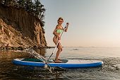 Young woman standing on inflatable sup board and paddling through water