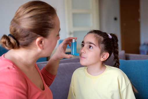 Mother teaching her little daughter how to use asthma inhaler