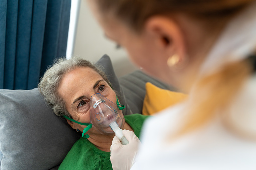 Doctor helping senior woman to put nebulizer inhaler face mask at home