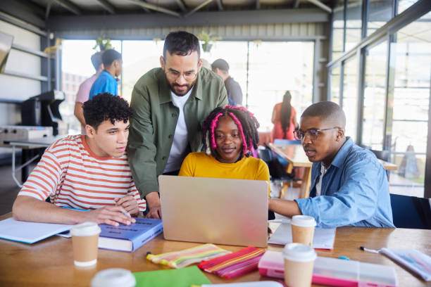 istock Teacher helping students working together on a laptop in a college cafeteria 1889223040