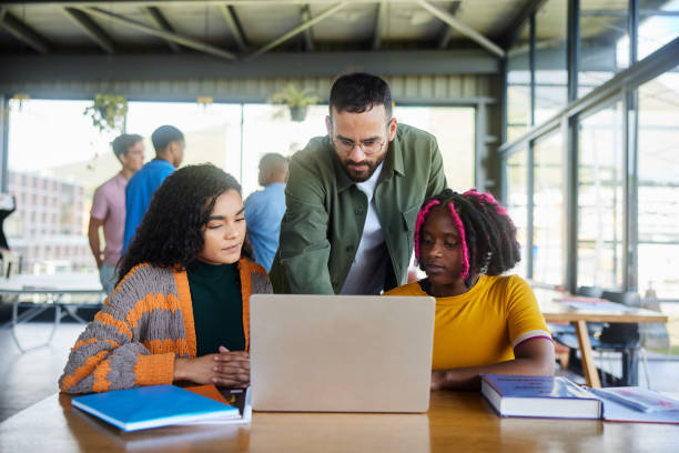 istock Teacher helping female college students working on a laptop in a cafeteria 1889227743