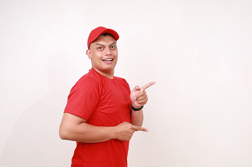Handsome young asian courier standing while pointing sideways against white background