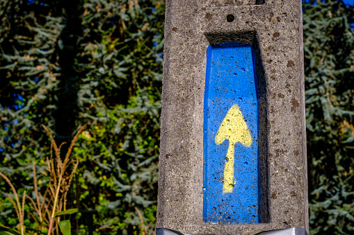 Cement post with a yellow arrow on a blue background, indicating the Camino de Santiago in Galicia (Spain)