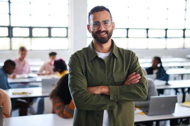 istock Smiling college teacher standing in a class with students in the background 1889240701