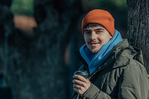 portrait young man bundled up in winter outdoors with cup of coffee