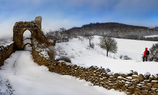 A walker on a snow covered hillside near the ruins of a castle in the Highlands of Scotland.