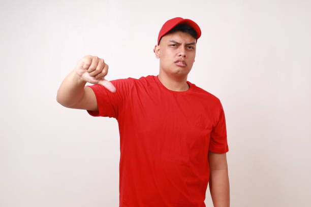 istock Handsome young asian courier standing while making thumbs down or dislike against white background 1889266988