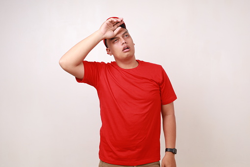 Tired young asian courier standing while holding head against white background