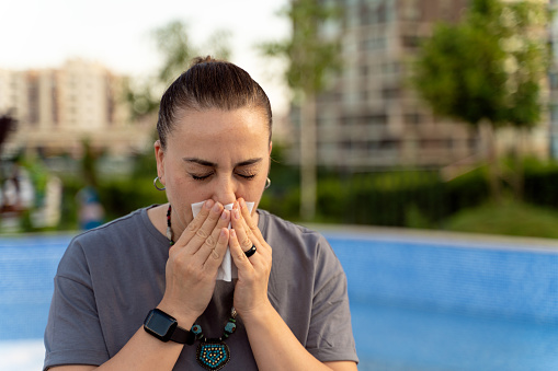 Woman sneezing due to allergies outdoors