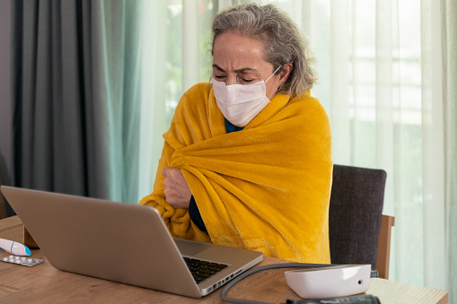 Senior woman with flu and cold possibility asking her doctor for help from her home with laptop
