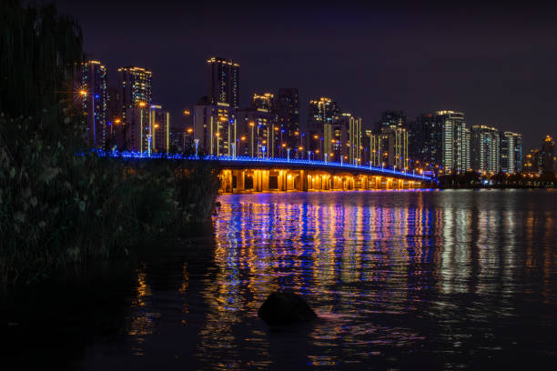 Illuminated bridge in Suzhou, China during nighttime. The city’s skyline forms the backdrop, with lights reflecting off the water.