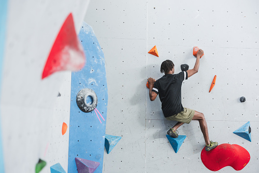 Athletic African American man climbing in a colorfull indoor wall. Extreme sports and bouldering concept, in monochrome.