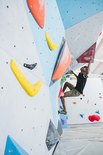 Athletic African American man climbing in a colorfull indoor wall. Extreme sports and bouldering concept, in monochrome.