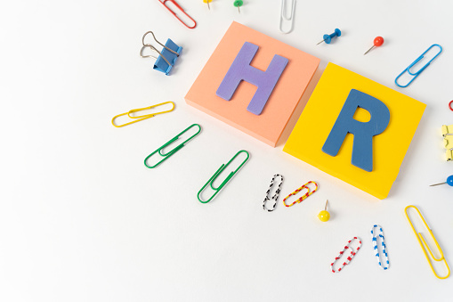Management abbreviation HR made with letters on light color background. HR, Human Resource department, hiring new job or position in company concept. Work equipment, paper clips.