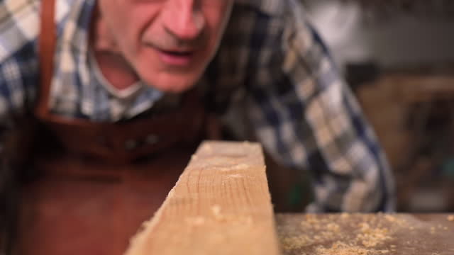 Slow motion Carpenter blowing sawdust away from handcrafted wood plank on workbench. Artisan worki . Build home creative ideas. High quality Full HD footge