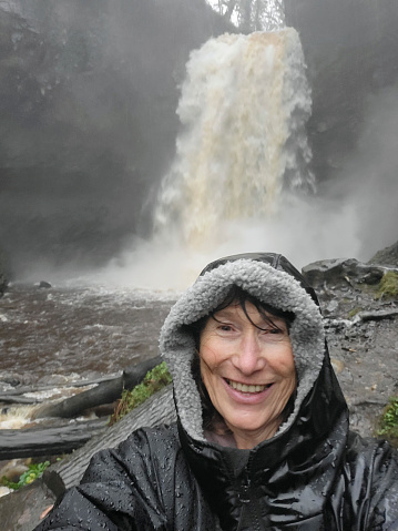 Mature woman takes a selfie at Henrhyd Falls after torrential rainfall - one of the many waterfalls in Waterfall Country, near Pontneddfechan. Henrhyd is the tallest waterfall in southern Wales with a drop of 90 feet.