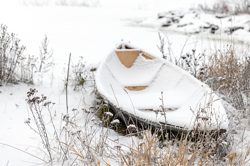 An empty row boat covered with snow lays on the coast of Baltic Sea on a winter day