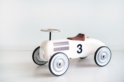 A little white retro toy car placed on a white vinyl floor in a home. This scene is symbolic of childhood, toys, and imaginative play. It evokes a sense of nostalgia and simplicity, reflecting the joy and creativity associated with children's playtime.